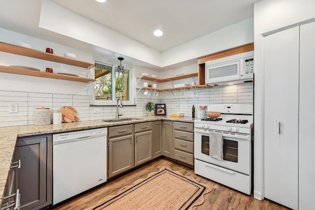 kitchen featuring tasteful backsplash, light stone countertops, sink, and white appliances