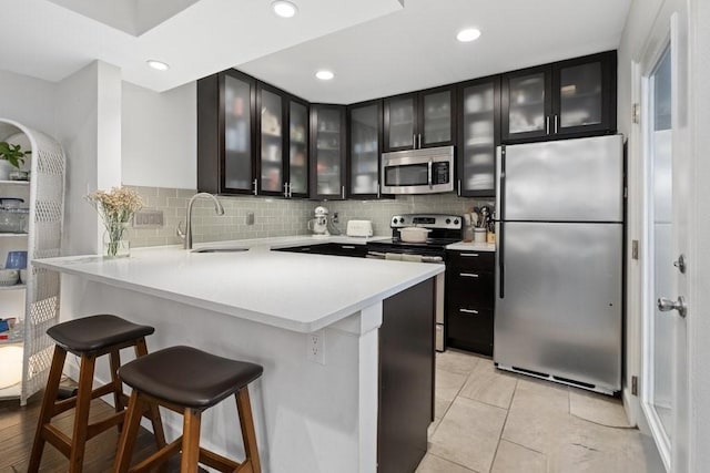 kitchen with appliances with stainless steel finishes, backsplash, sink, a kitchen bar, and kitchen peninsula