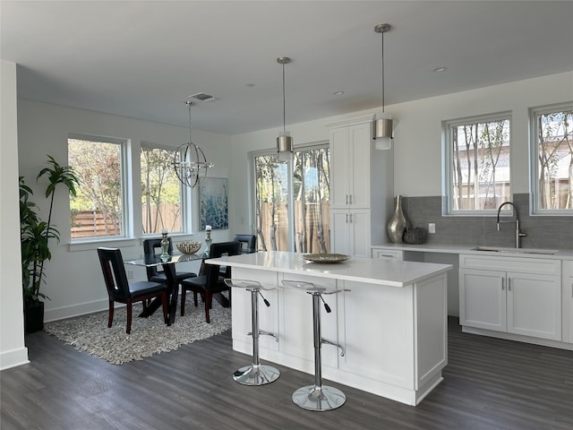 kitchen with dark wood-type flooring, sink, decorative light fixtures, a center island, and white cabinets