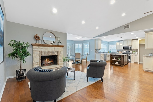 living room with lofted ceiling, a fireplace, and light hardwood / wood-style flooring