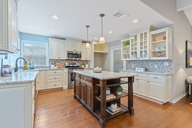 kitchen with sink, appliances with stainless steel finishes, hanging light fixtures, light stone countertops, and a kitchen island