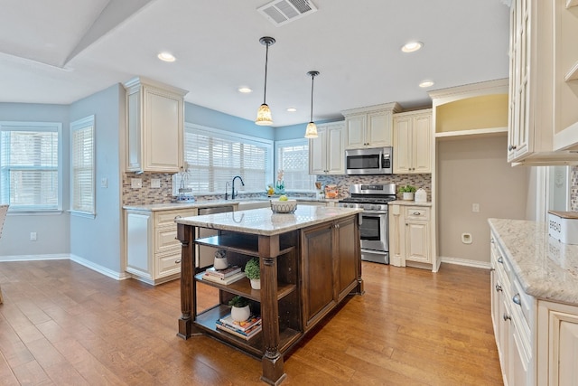 kitchen with a kitchen island, appliances with stainless steel finishes, hanging light fixtures, light stone counters, and cream cabinetry
