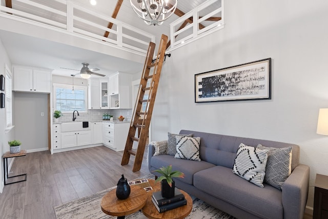 living room with ceiling fan with notable chandelier, light hardwood / wood-style floors, and sink