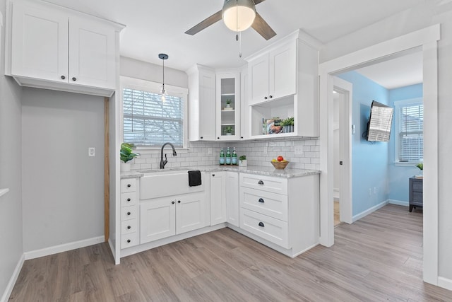 kitchen with light stone counters, sink, decorative light fixtures, and white cabinets