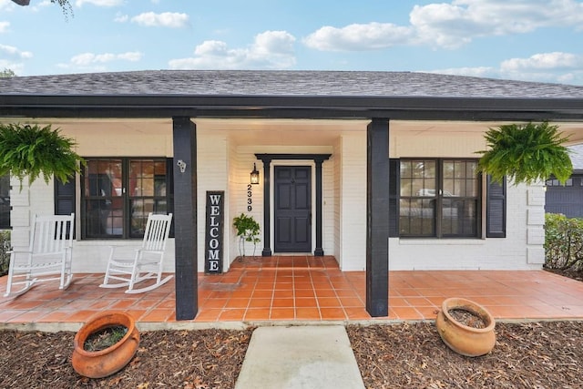 doorway to property with brick siding, covered porch, and a shingled roof