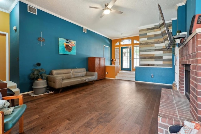 living room with wood finished floors, visible vents, a fireplace, a textured ceiling, and crown molding