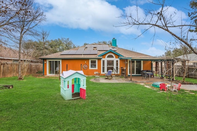 back of house featuring a fenced backyard, a chimney, solar panels, a patio area, and a yard