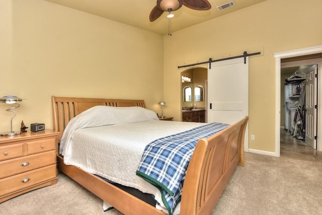 bedroom with connected bathroom, a walk in closet, light colored carpet, ceiling fan, and a barn door