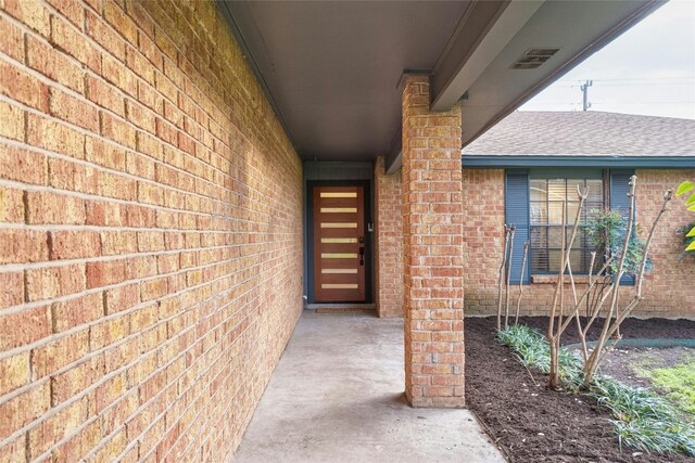 property entrance featuring brick siding and a shingled roof