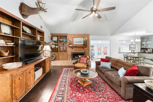 living area with a brick fireplace, built in shelves, ceiling fan with notable chandelier, french doors, and dark wood-style floors