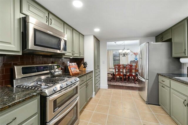 kitchen featuring light tile patterned floors, green cabinetry, decorative backsplash, appliances with stainless steel finishes, and a notable chandelier