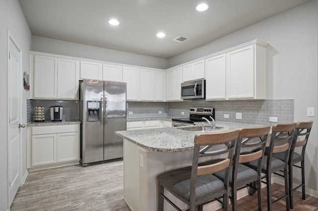 kitchen with white cabinetry, appliances with stainless steel finishes, a kitchen breakfast bar, and kitchen peninsula