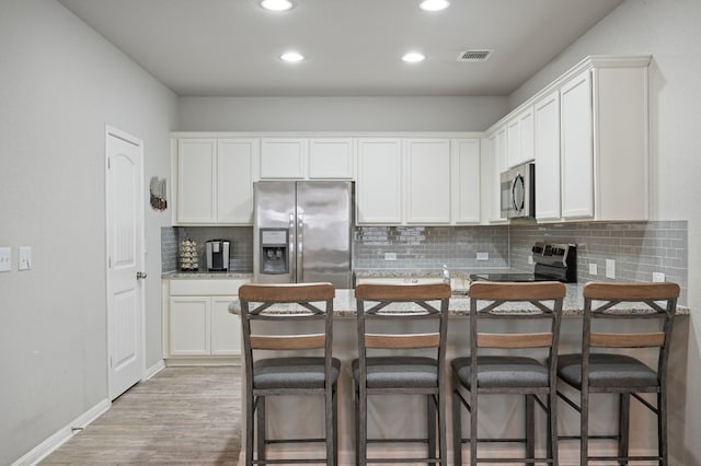 kitchen featuring tasteful backsplash, white cabinetry, a kitchen breakfast bar, stainless steel appliances, and light hardwood / wood-style flooring