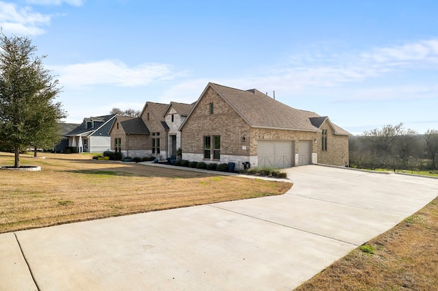 french country inspired facade featuring brick siding, a shingled roof, concrete driveway, an attached garage, and a front yard