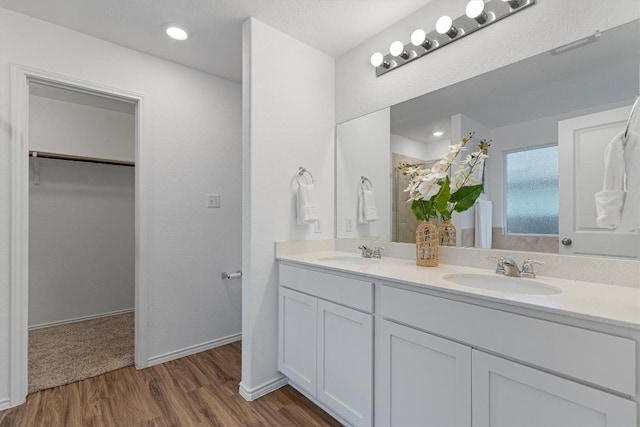 full bath with double vanity, a sink, a spacious closet, and wood finished floors