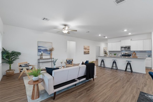 living area with wood finished floors, visible vents, and a ceiling fan