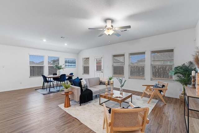 living room featuring light wood-style floors, visible vents, baseboards, and a ceiling fan