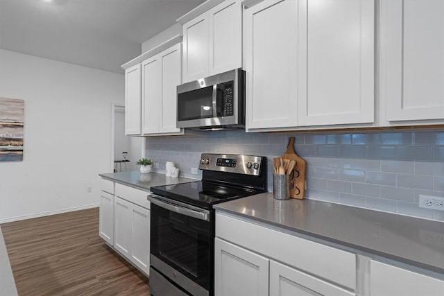 kitchen with dark wood finished floors, dark countertops, decorative backsplash, appliances with stainless steel finishes, and white cabinetry