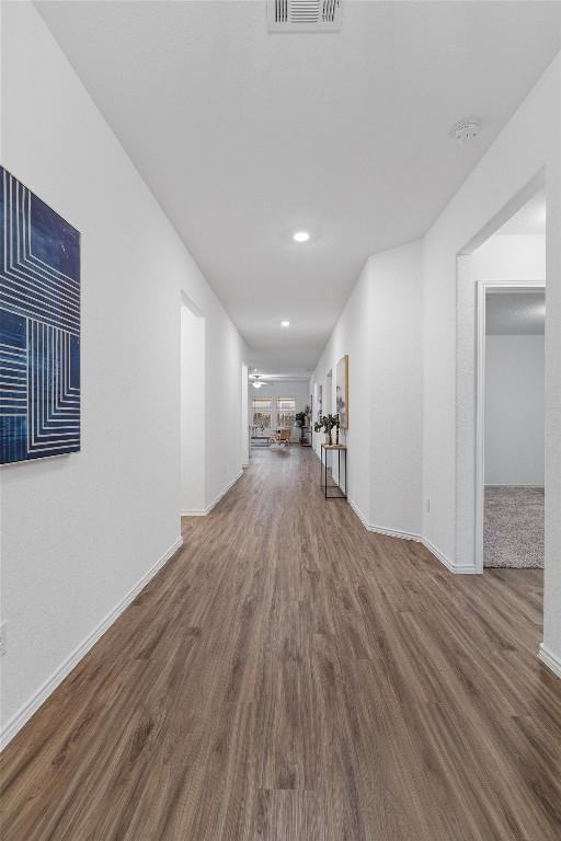 hall with wood finished floors, visible vents, and baseboards