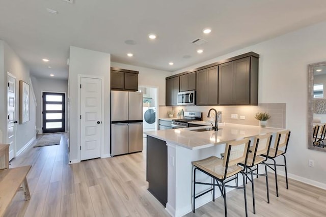 kitchen with sink, a breakfast bar area, appliances with stainless steel finishes, kitchen peninsula, and light wood-type flooring