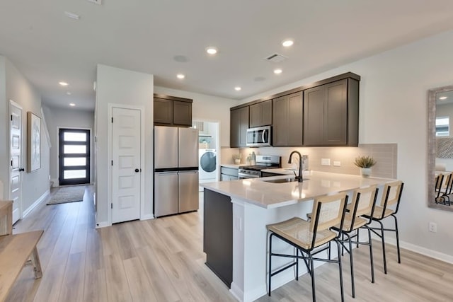 kitchen with appliances with stainless steel finishes, sink, a kitchen breakfast bar, kitchen peninsula, and light wood-type flooring