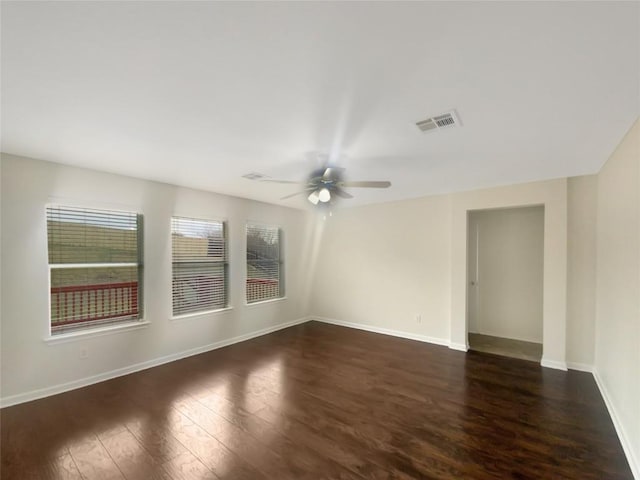 spare room featuring dark wood-style floors, a ceiling fan, visible vents, and baseboards