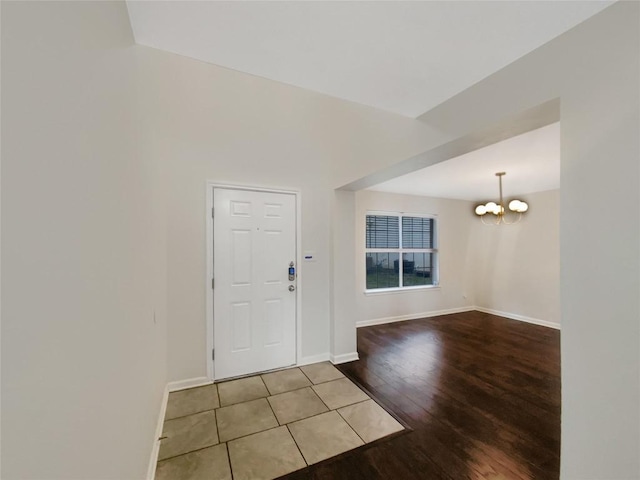 entryway featuring light wood-type flooring, lofted ceiling, baseboards, and an inviting chandelier