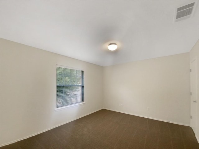 spare room featuring dark colored carpet, visible vents, and baseboards