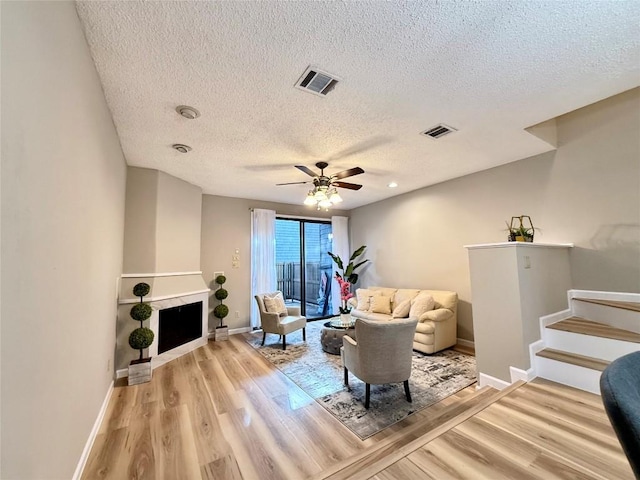 living room with a textured ceiling, ceiling fan, and light wood-type flooring