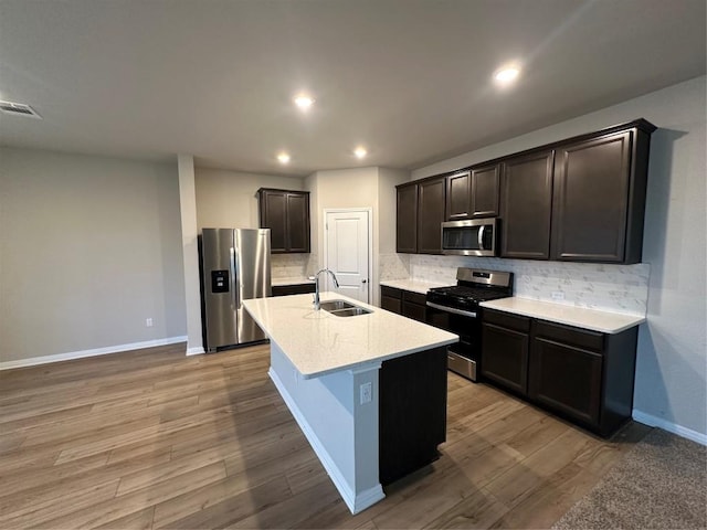 kitchen with sink, light hardwood / wood-style flooring, appliances with stainless steel finishes, backsplash, and a center island with sink