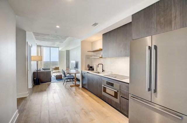 kitchen featuring sink, light hardwood / wood-style flooring, expansive windows, and appliances with stainless steel finishes