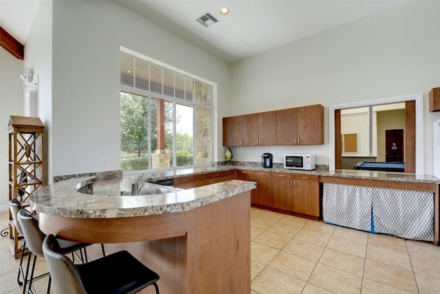 13701 Glen Mark Dr, Manor, TX 78653 - kitchen featuring white microwave, light tile patterned floors, brown cabinets, a peninsula, and a kitchen breakfast bar