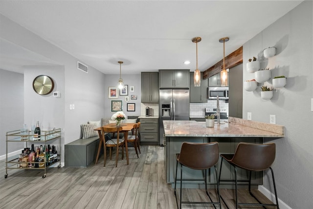 kitchen featuring gray cabinetry, light stone counters, appliances with stainless steel finishes, kitchen peninsula, and backsplash