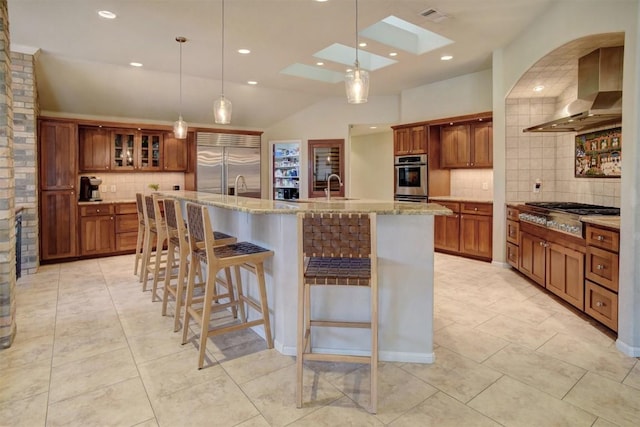 kitchen featuring wall chimney range hood, a breakfast bar, appliances with stainless steel finishes, hanging light fixtures, and a spacious island