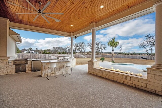 view of patio with ceiling fan, an outdoor kitchen, a jacuzzi, fence, and grilling area