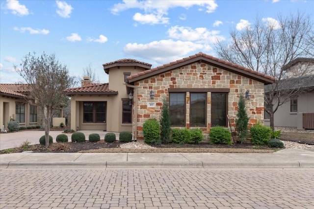 mediterranean / spanish house with stone siding, a tile roof, a chimney, and stucco siding