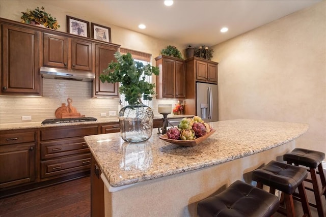 kitchen featuring dark wood-type flooring, appliances with stainless steel finishes, backsplash, a center island, and light stone countertops