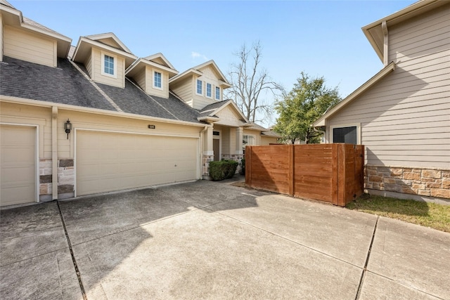 exterior space featuring stone siding, a shingled roof, fence, and driveway