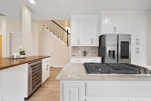 1302 Olympus Dr, Austin, TX 78733 - kitchen with beverage cooler, stainless steel appliances, light wood-style floors, a center island, and butcher block counters