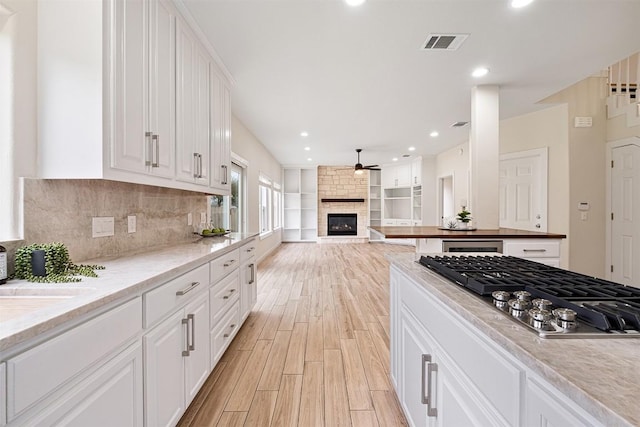 1302 Olympus Dr, Austin, TX 78733 - kitchen featuring stainless steel gas stovetop, light wood-type flooring, a ceiling fan, white cabinets, and a fireplace