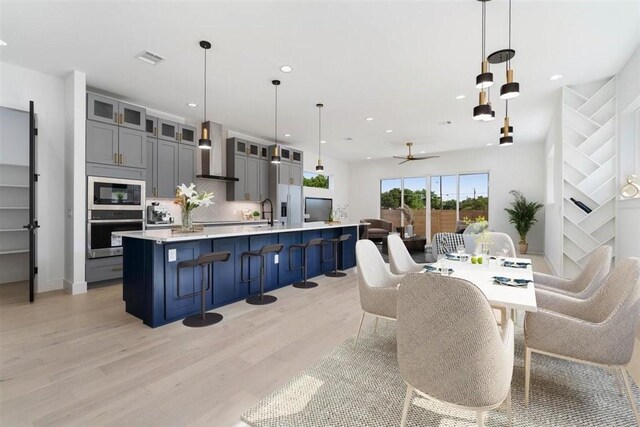 501 E Burton St, Manor, TX 78653 - kitchen featuring stainless steel appliances, wall chimney exhaust hood, light wood-type flooring, light countertops, and glass insert cabinets