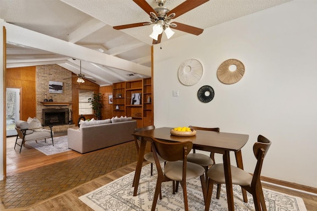 dining area featuring a fireplace, lofted ceiling with beams, ceiling fan, a textured ceiling, and light wood-type flooring