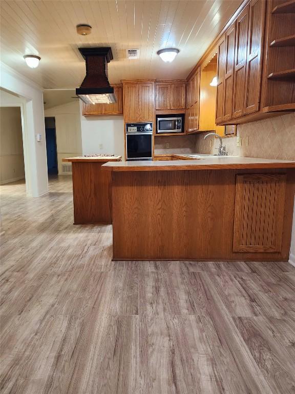 kitchen featuring custom exhaust hood, oven, light wood-type flooring, and kitchen peninsula