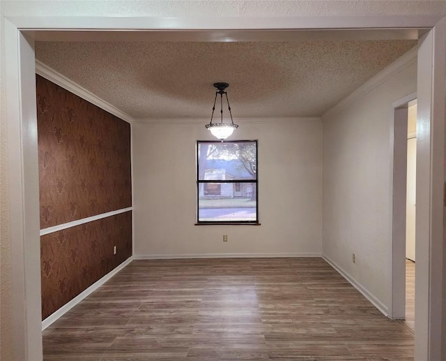 empty room with crown molding, wooden walls, a textured ceiling, and hardwood / wood-style flooring