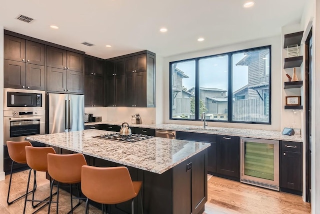 19217 Lost Tree Cv, Spicewood, TX 78669 - kitchen with wine cooler, stainless steel appliances, a kitchen island, light stone countertops, and a kitchen bar