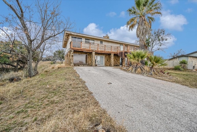 coastal home with a deck, driveway, and a chimney