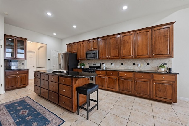 kitchen with a kitchen bar, tasteful backsplash, light tile patterned floors, appliances with stainless steel finishes, and a kitchen island