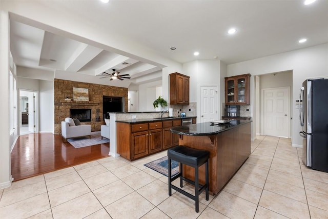 kitchen with a stone fireplace, dark stone counters, light tile patterned floors, kitchen peninsula, and stainless steel appliances