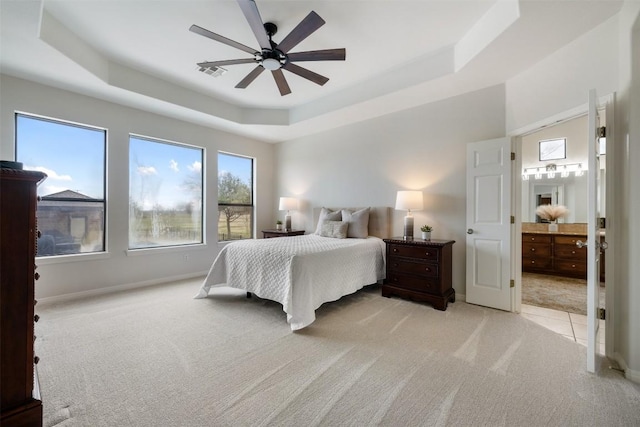 carpeted bedroom featuring a tray ceiling, ensuite bath, and ceiling fan