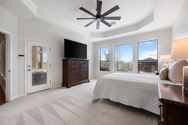 bedroom featuring multiple windows, access to exterior, light colored carpet, and a raised ceiling